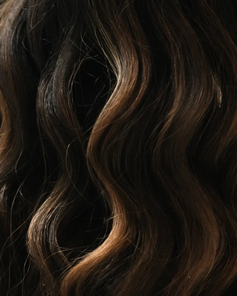 Detalhe de cabelo castanho ondulado com reflexos